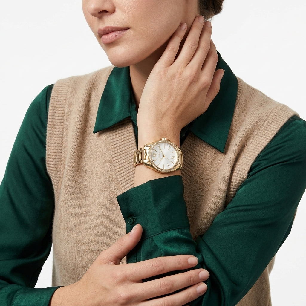 A close-up of a woman wearing a gold-tone watch with a white dial and bracelet, styled with a green collared shirt and a beige knit vest against a clean white background.