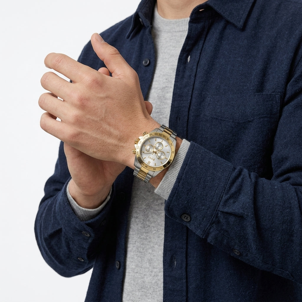A close-up of a man wearing a gold and silver two-tone watch with a white dial, styled over a gray crewneck sweater and a navy blue button-up shirt.