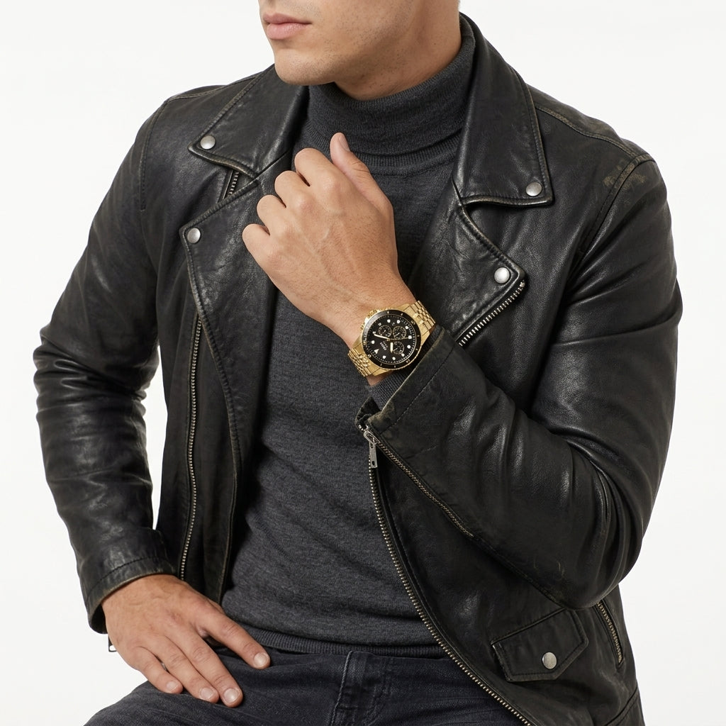 A man wearing a black leather motorcycle jacket over a dark gray turtleneck, accessorized with a gold-tone watch with a black dial on his wrist, set against a plain white background.