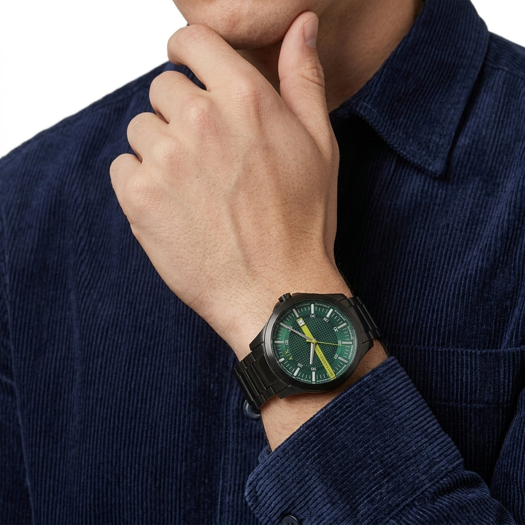 A close-up of a man wearing a black watch with a green dial and yellow hands, shown on his wrist while wearing a dark blue corduroy shirt.