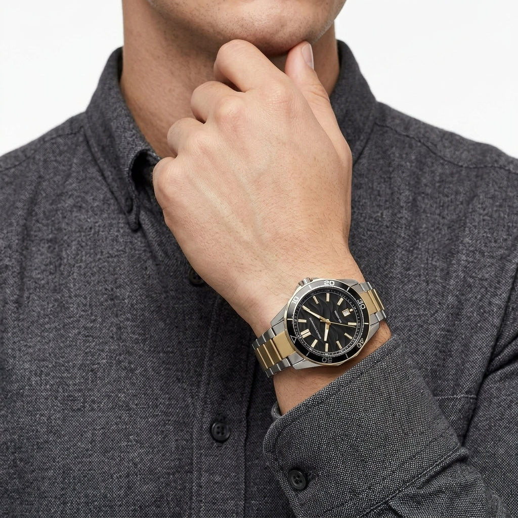 A close-up of a man wearing a two-tone stainless steel and gold watch with a black dial, paired with a dark gray textured button-down shirt.