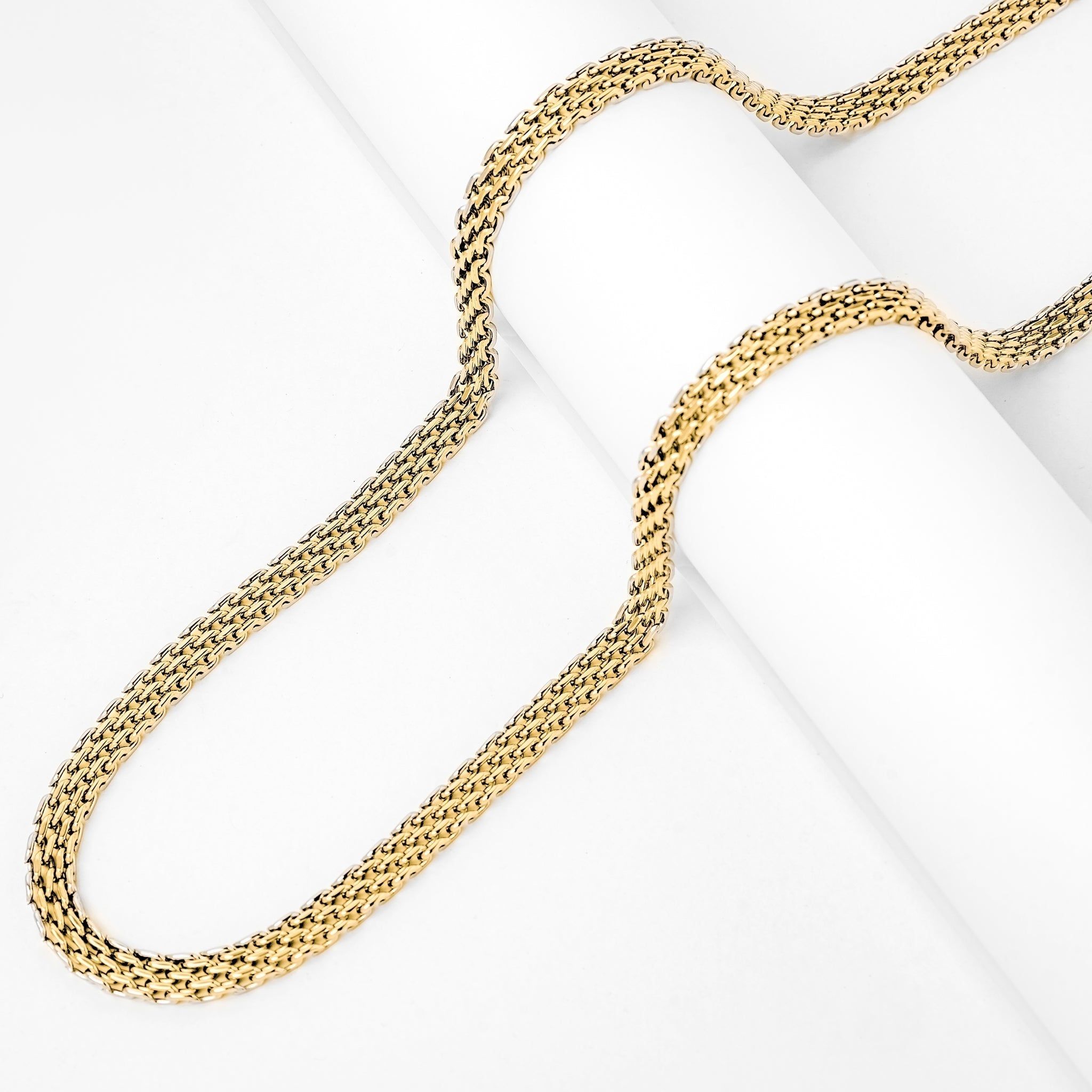 Multiple 6MM gold flat herringbone chains laying flat on white surface