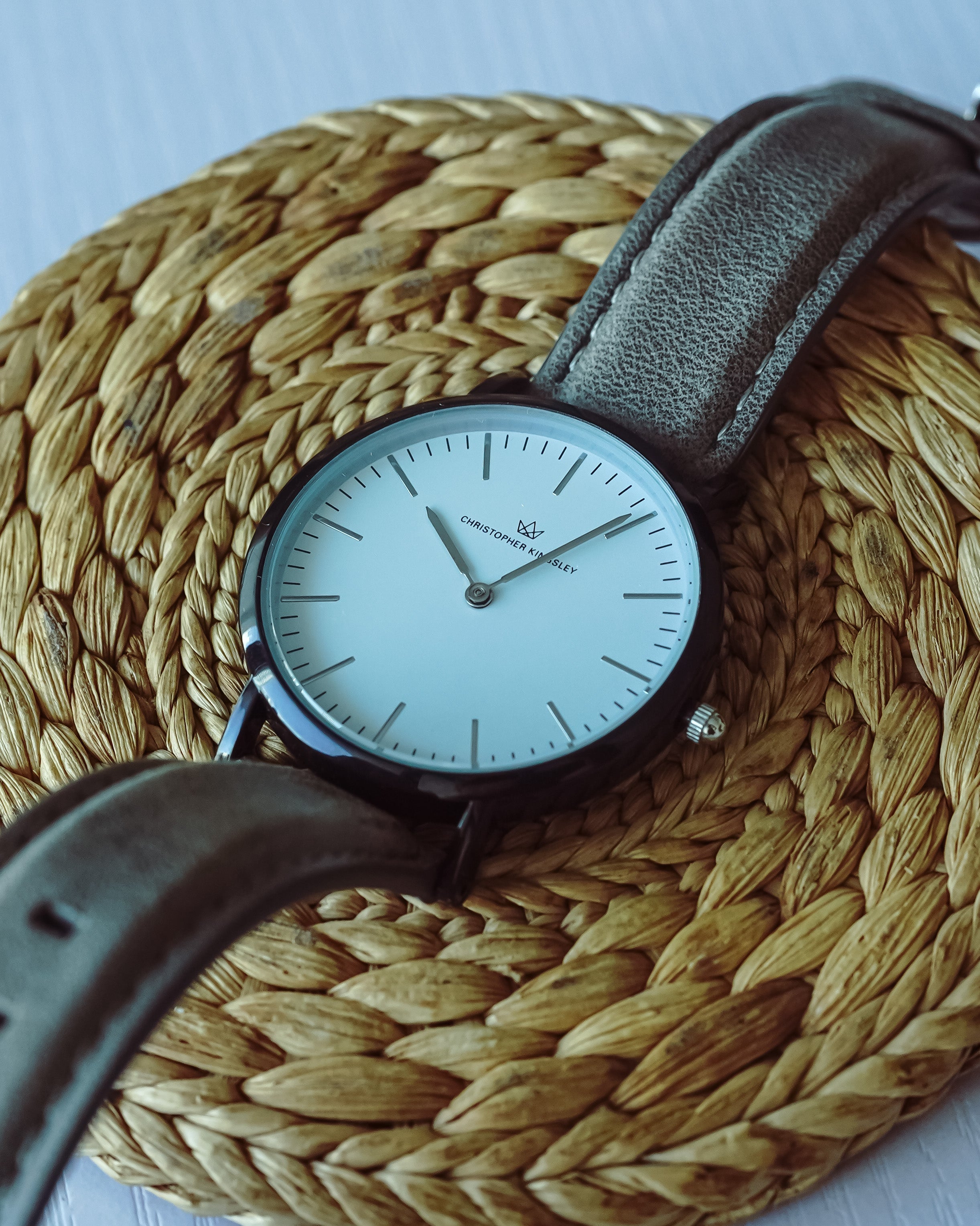 Christopher Kingsley watch worn on wrist with grey leather strap on woven background